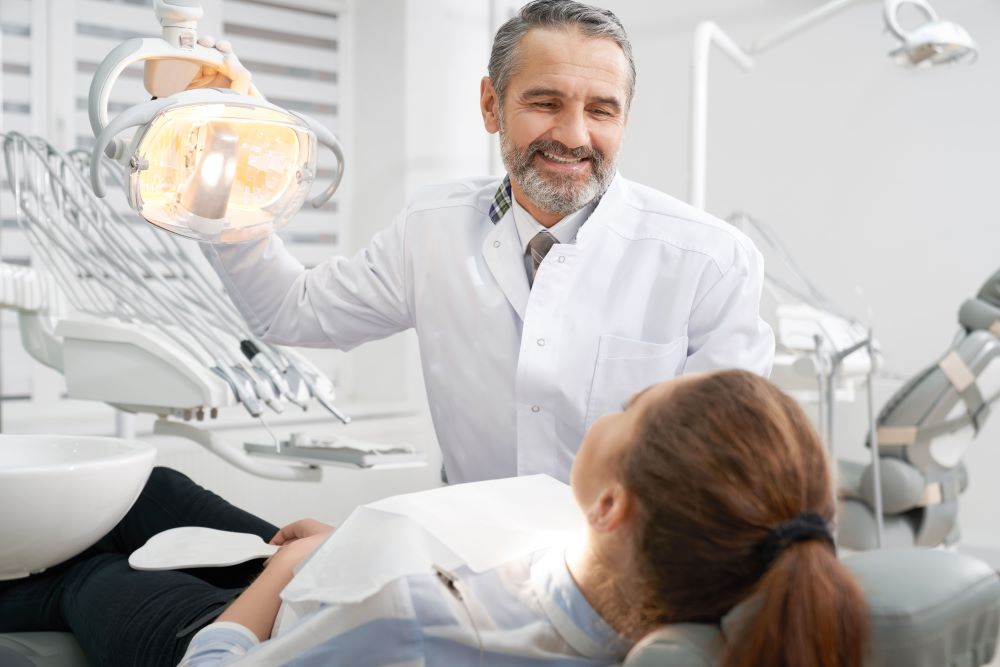 cheerul-dentist-smiling-looking-at-patient-W8ASD5W